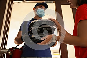 Courier in protective mask and gloves giving order to woman at entrance. Restaurant delivery service during coronavirus quarantine