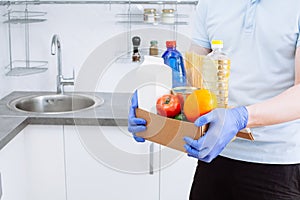Courier in protective medical gloves delivers box with set food stock for quarantine isolation period. Online food store and
