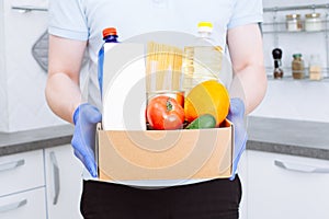 Courier in protective medical gloves delivers box with set food stock for quarantine isolation period. Organic food and products