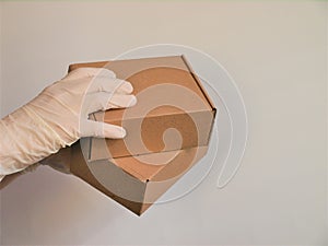 Courier`s hands in latex white medical gloves deliver parcels in brown cardboard boxes to the door during the epidemic of