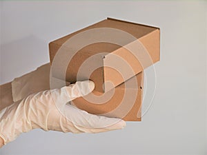 Courier`s hands in latex white medical gloves deliver parcels in brown cardboard boxes to the door during the epidemic of