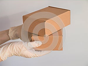 Courier`s hands in latex white medical gloves deliver parcels in brown cardboard boxes to the door during the epidemic of