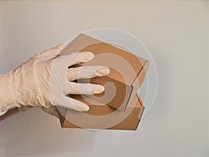 Courier`s hands in latex white medical gloves deliver parcels in brown cardboard boxes to the door during the epidemic of