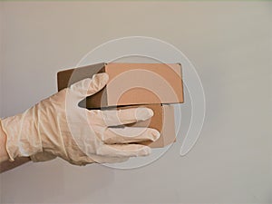 Courier`s hands in latex white medical gloves deliver parcels in brown cardboard boxes to the door during the epidemic of