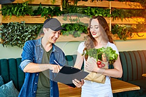 Courier service worker delivering fresh food, giving shopping bag to a happy woman client on the kitchen at home. Online grocery