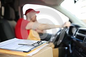 Courier in uniform in car and receipt documents on clipboard for client