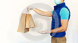 Courier in uniform face mask gloves reaching out hand with paper packages or bags n front of white background.