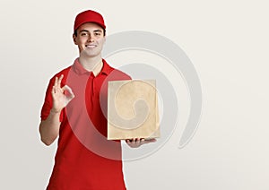 Courier in uniform holds paper package and shows symbol ok with hand