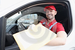 A courier in a uniform sitting in a car holds out a package