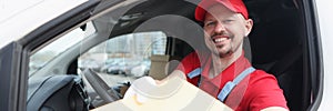 A courier in a uniform sitting in a car holds out a package