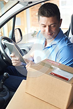 Courier In Van With Digital Tablet Delivering Package To Domestic House