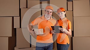 Couriers in orange uniform standing against brown carton stacks backround. Delivery company staff