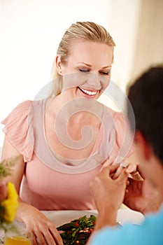 Of course Ill marry you. A beautiful woman smiling as her fiancee slips a ring on her finger.