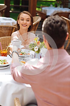 Courteous dark-haired man giving cup of tea to his girlfriend photo