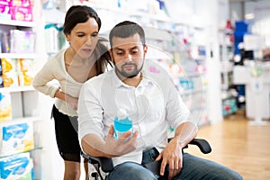 Courteous woman helping man in a wheelchair to choose the right medicine in pharmacy photo