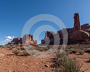 Red dirt and sagebrush views of the Courthouse Towers in Arches National Park on a Sunny Blue Sky day photo