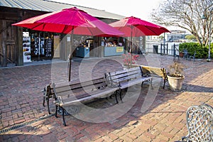 A courtyard with benches, black metal tables and chairs, red umbrellas, red flowers, and lush green plants along the Savannah