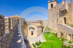 Courtyard with green grass lawn of Prima Torre Guaita first medieval tower with stone brick fortress wall with merlons, San Marino