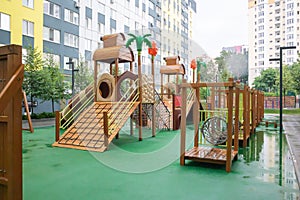 A courtyard of high-rise buildings with a modern and large playground made of wood and plastic on a rainy summer day without