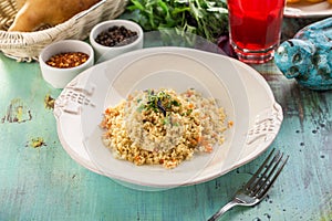 Cous cous with carrot in white bowl with glass of red drink on blue wooden table