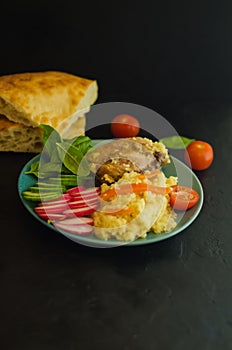 Cous cous with chicken and vegetables and greens on a black background near Eastern pita bread