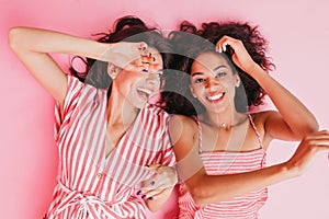 Cousins in wonderful mood are lying on floor in high spirits. Girls pose with sincere smiles in pin