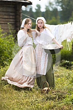 Coutryside Lifestyle. Portrait of Two Lovely Country Girls Posing Together With Basin Outdoor With Linens Sheets Hanged On Rope