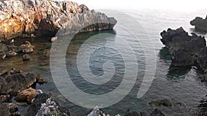 A cove along the cliffside with indented rocks and a stony seafloor at sunset. Inlet.