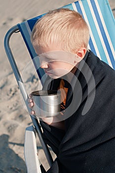 Covered with a blanket boy drinking from a steel cup