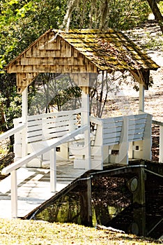 A covered bridge in a garden with two bench seats.