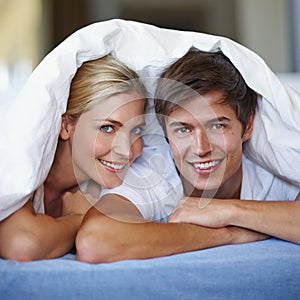 Covered in love. a happy young couple enjoying a playful moment underneath the duvet.