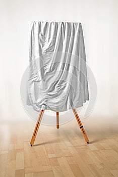 Covered painting on an easel, white cloth over the picture, wood photo