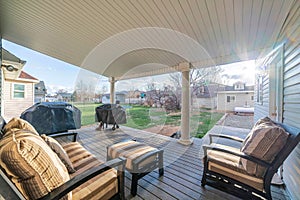 Covered patio of a house with wooden couch and two covered grills