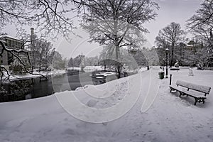 Covered in snow bench and canal in winter park. Winter landscape in snowy park with beautiful small canal and covered in snow