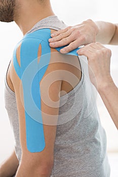 Physiotherapist covering selected fragments of young man`s body with special structure patches during kinesiotaping therapy photo