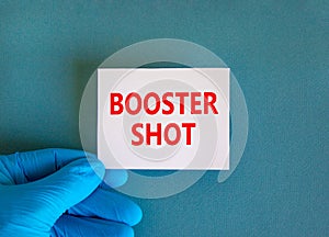 Covid-19 booster shot vaccine symbol. White note with words booster shot, beautiful blue background, doctor hand in blue glove.