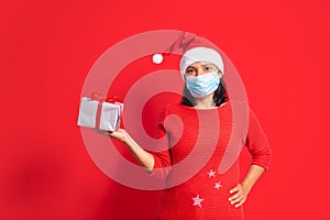 Covid-19 christmas concept. young happy woman offering boxes of gifts, face mask, santa claus outfit smiling on light blue