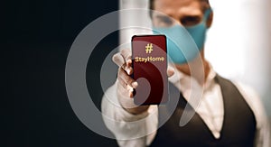 Covid-19 or Corona Virus Situation Concept. Young Man with Medical Mask presenting a Hashtag Sign to Stay Home on Smartphone