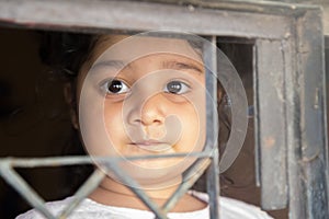 COVID-19 coronavirus concept, little girl in looking through window at home. Sad kid during quarantine due to COVID