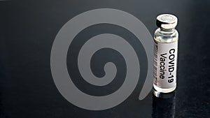 COVID-19 coronavirus vaccine background, bottle with vaccine for SARS-CoV-2 coronavirus cure on black desk