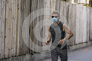 Covid-19 deconfinement - young attractive and happy man outdoors doing running workout in the city wearing protective face mask