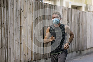 Covid-19 deconfinement - young attractive and happy man outdoors doing running workout in the city wearing protective face mask