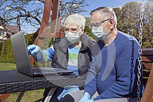 COVID 19 An elderly couple a man and a woman in medical masks in front of a laptop in a garden in a nursing home