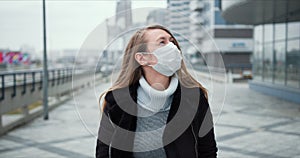 COVID-19 epidemic protection. Young blonde woman in medical face mask walks along empty city street during lockdown.