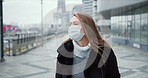 COVID-19 epidemic protection. Young blonde woman in medical face mask walks along empty city street during lockdown.
