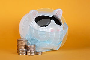 Covid-19 financial crisis. Coronavirus crisis, white piggy bank with face mask stuffed with coin on yellow background