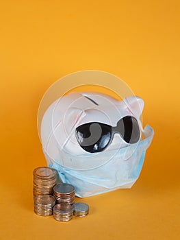 Covid-19 financial crisis. Coronavirus crisis, white piggy bank with face mask stuffed with coin on yellow background