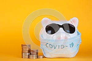 Covid-19 financial crisis. Coronavirus crisis, white piggy bank with face mask stuffed with coin on yellow background