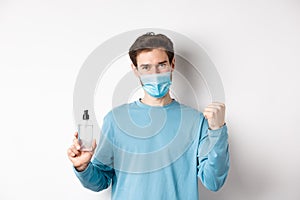 Covid-19, health and quarantine concept. Cheerful man in face mask celebrating, showing fist pump and bottle with hand