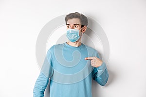 Covid-19, health and quarantine concept. Confused man in medical mask pointing at himself, looking left with ambushed